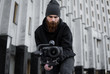 © Volodymyr - Bearded Professional videographer in black hoodie holding professional camera on 3-axis gimbal stabilizer. Filmmaker making a great video with a professional cinema camera. Cinematographer.