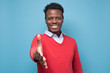 © Viktor Koldunov - Young african american man reaching out toward camera to shake hands on blue background