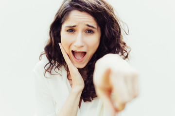 Wall Mural - Excited student girl pointing index finger at camera, laughing, mocking. Wavy haired young woman in casual shirt standing isolated over white background. Pointing at you concept