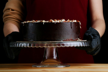 Wall Mural - Chocolate raw cake with jam filling with hazelnuts on wooden table. vegan dessert closeup. woman confectioner hold chocolate cake with nuts. gloved hands of a pastry chef