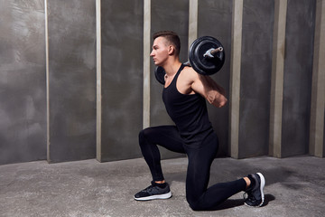 man in black sports uniform with dumbbells on a background of gray wall