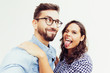© Mangostar - Joyful funny couple grimacing for selfie, smiling and sticking tongue out. Young woman in casual and man in glasses standing isolated over white background. Couple having fun concept