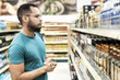 © Mangostar - Focused African American man choosing alcohol drinks. Serious bearded guy standing in aisle and looking at drinks. Shopping concept