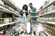 © Mangostar - Focused young couple standing in aisle with alcohol drinks. African American people making purchases according to shopping list. Shopping concept