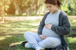 © boyloso - Portrait of young Asian pregnant woman holding her belly during relax in the park. Conceptual shot of healthy pregnant woman feeling.