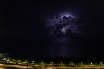 Wall Mural - An intense thunderstorm cloud with blue or purple colors and lit up with numerous lightning strikes moves over Lake Michigan as cars pass by on Lake Shore Drive on Chicago's north side.