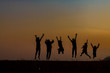 The silhouette of the children holding hands, enjoying the sunset, a group of friends cheering and arms raised in the orange sky and the mountains behind Friendship concept
