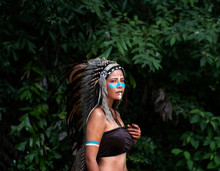 The Beautiful Woman Wearing Headdress Feathers Of Birds.paint Body With Brown Color And Face With Blue Color,model Posing In Forest,vintage And Art Style
