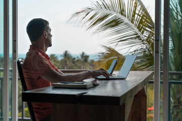 Man works at home at a wooden table with a laptop and smartphone