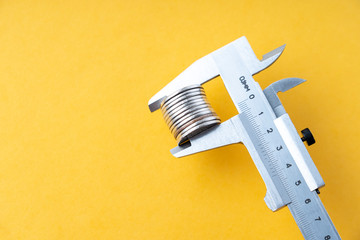 coins in a caliper, business concept of measuring profit and loss, selective focus on an orange background