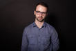 © Xristoforov - Attractive brunette man in glasses confidently looks at camera. Black backgroung