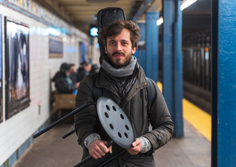 portrait of a man  Guitarist busker inside the new york city subway metro holding a stool with a guitar on his shoulders inside a soft gig bag Manhattan NYC