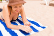 © sosiukin - Girl is relaxing on the towel on the sand at the beach and applying sun lotion on her hand