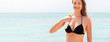 © sosiukin - Smiling woman is applying sun cream from the spray on her body at the sea background