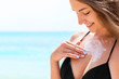 © sosiukin - Young attractive woman is protecting her skin on the breast with sunblock at the sunny beach