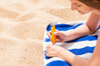 © sosiukin - Attractive woman is lying on a striped towel at the beach and squeezing sunblock from a tube on her hand