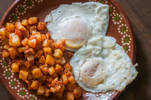 Over Medium Eggs With Potatoes And Chorizo On The Side On A Mexican Clay Or Mud Plate On A Wooden Table As Part Of A Complete Mexican Breakfast.