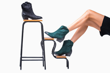 green and black cossack boots leather with a brown heel are dressed which stand on the stand on a model that sits, on a white background. fashionable footwear. studio shooting. harmonious legs.