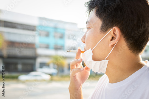 Asian man with a protective mask during Covid-19 pandemic,hold a cigarette in his mouth,smokers male smoking,spreading of Coronavirus with droplets come out from smoke of cigarette,airborne diseases
