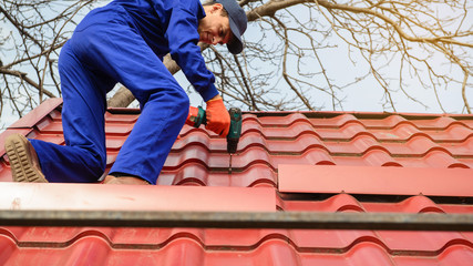 Wall Mural - Young man worker in blue overall fix a metal tile roof