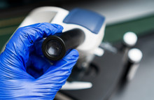 Hand In Glove Holding Microscope Eyepiece In Laboratory.