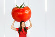 Young hunger pretty funny woman holds huge and large red tomato with drops water. Girl walks with big heavy vegetable