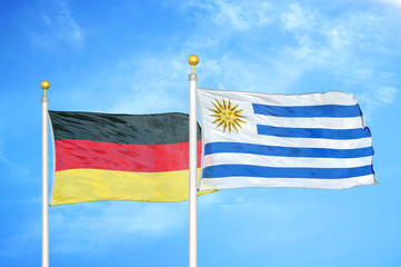 Germany and Uruguay two flags on flagpoles and blue cloudy sky