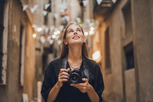 Outdoor Summer Smiling Lifestyle Portrait Of Pretty Young Woman Having Fun Taking Pictures In The City During Her Travel. She Is Using Professional Photo Camera And Looking Around Beautiful Streets