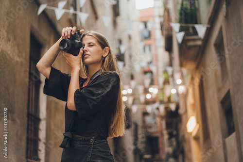 Plakat Fotografka turystyczna próbuje uchwycić chwilę, wzięła aparat fotograficzny, przycisnęła go do twarzy i zaczęła robić zdjęcia. Ona uśmiecha się i cieszy na ulicach miasta