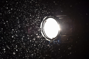 Illuminated snowflakes are seen in the light of a professional spotlight lamp at night during heavy snowfall