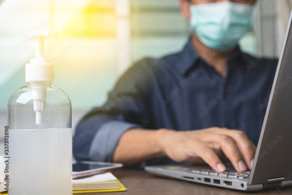 Alcohol gel with male employee wearing a health mask Preventing corona virus infection covid-19 in back, concept of working from home and social distancing. - obrazy, fototapety, plakaty 