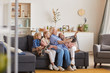 © AnnaStills - Grandmother sitting on sofa together with her grandchildren and they making a selfie on mobile phone during home party