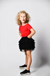 Frolic little kid girl in black skirt and red t-shirt poses with her hands on hips, sticking her tongue out at us
