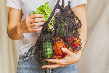 Wall Mural - Girl holding mesh shopping bag full of vegetables and taking from inside a fresh lettuce from the farm. Sustainable, zero waste and plastic free lifestyle. Save the planet concept