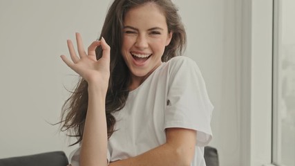 Wall Mural - Happy pretty brunette woman showing ok sign and looking at the camera at home