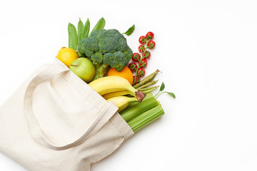 Zero waste food shopping with reusable bags. Flat lay with fruits and vegetables in textile tote bag isolated on white background with copyspace.