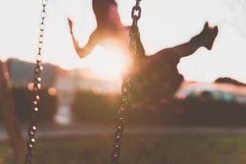 Girl having fun on the swing - young millenial woman relaxes in the park - freedom and well-being concetp - focus on the chain with blurred background