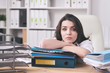 © pressmaster - Young unhappy female accountant or secretary lying on thick stack of papers