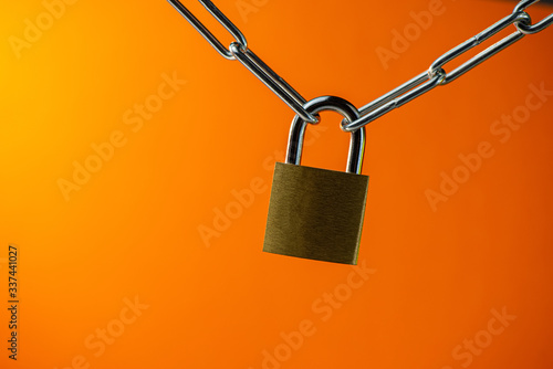 Photographie padlock connecting a metal chain on an orange background