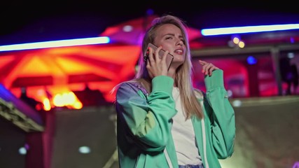 Wall Mural - A smiling positive young woman is talking on the phone while trying to find someone at the disco party at night