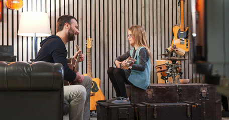 Wall Mural - Dad teaching guitar and ukulele to his daughter.Little girl learning guitar at home.Side view.Ukulele class at home. Child learning guitar from her father