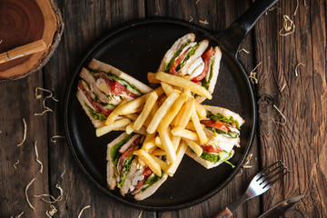Wall Mural - Top view on sandwiches with fries on the black pan on the wooden table, horizontal format