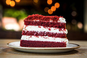 Wall Mural - Side view closeup on a piece of red velvet cake on the wooden table with blurry bokeh background, horizontal