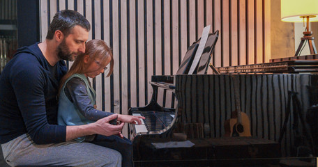 Wall Mural - Dad teaching piano to his daughter.Little girl learning piano at home.Side view.Piano class at home. Child learning piano from her father