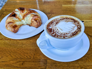 Fresh cappuccino and croissant on a wooden table