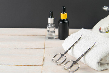 A set of cosmetic tools for manicure and pedicure on a blue background. Fraser, manicure scissors propped up to white towel, in the background are cuticoil oil and hand oil stand on a white wooden bac