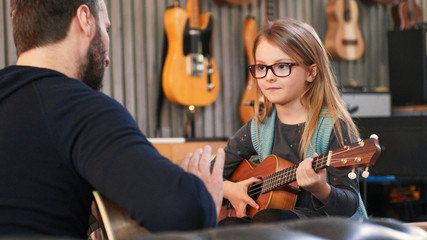 dad teaching guitar and ukulele to his daughter.little girl learning guitar at home.close up.ukulele