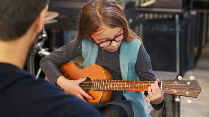 Wall Mural - Dad teaching guitar and ukulele to his daughter.Little girl learning guitar at home.Close up.Ukulele class at home. Child learning guitar from her father