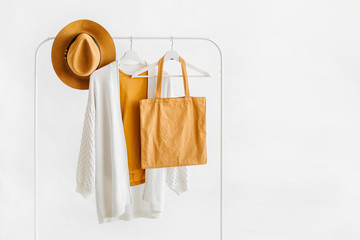 Wall Mural - White knitted jumper on hanger with brown hat and eco bag on white background. Elegant fashion outfit. Spring wardrobe. Minimal concept.