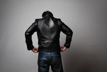 Portrait of man wearing leather jacket stands back in the studio. Horizontal.